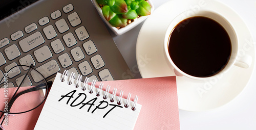 Office supplies, devices, coffee cup and glasses on white table with text ADAPT