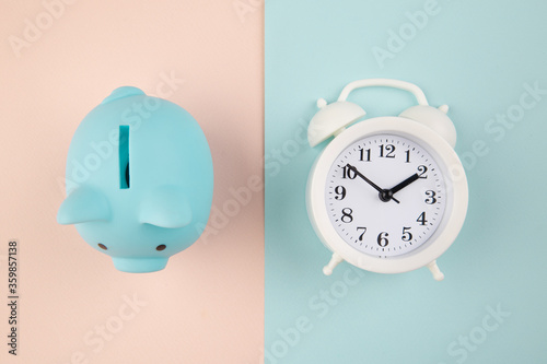 Time to invest. White clock and blue piggy bank on pink blue pastel background. photo