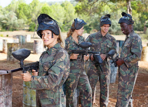 Young woman wearing uniform and holding gun ready for playing paintball with friends outdoor