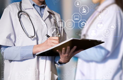 Doctor working with laptop computer and writing on paperwork. Hospital background.