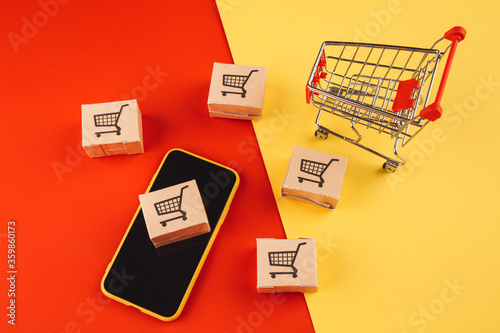 Online shopping concept. Boxes on smartphone and shopping cart isolated on colorful background.