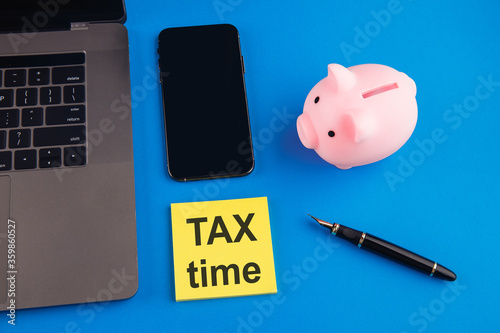 Tax time - notification of the need to file tax returns, tax form at accauntant workplace. Piggy bank in pink color with laptop and smartphone on blue background. photo