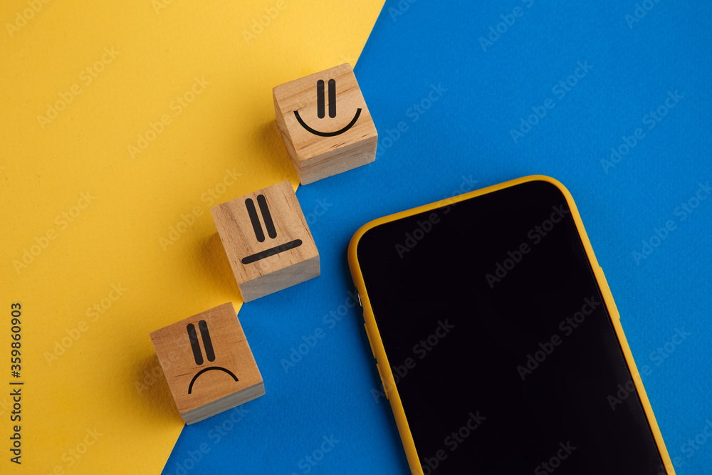 Obraz premium Emotion face symbol on wooden cube blocks and smartphone. Service rating, ranking, customer review, satisfaction and feedback concept.