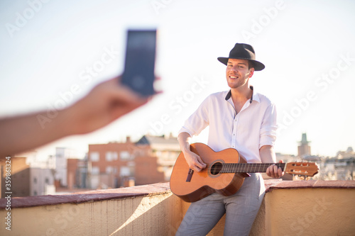 Joven cantante actuando por streaming en redes sociales en la azotea de un edificio al atardecer photo