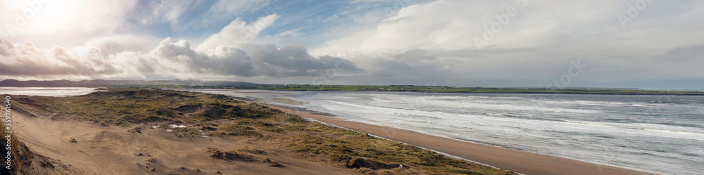 View on Strandhill beach and sand dunes, Sligo, Ireland. Panorama image, Warm sunny day, Cloudy sky, Atlantic ocean on the right. View on Strandhill beach and sand dunes, Sligo, Ireland. Panorama image, Warm sunny day, Cloudy sky, Atlantic ocean on the right.