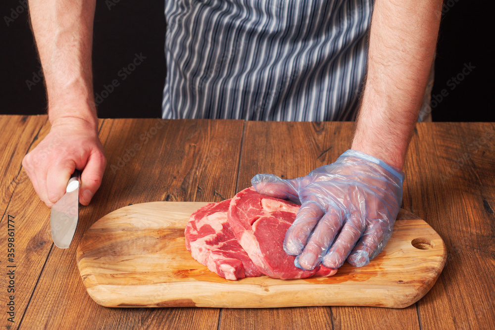 Butcher holding knife in his right hand. Two raw rib eye steaks on a wooden cutting board, Black background. Meat industry and proffesional at work concept.