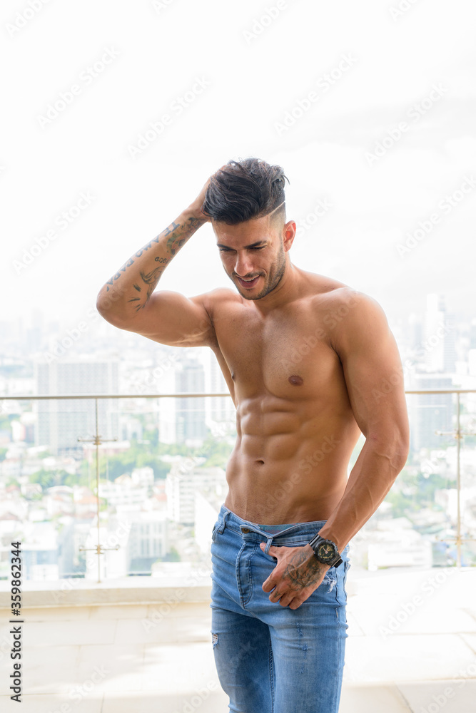 Fototapeta premium Happy young handsome muscular Persian man shirtless against view the city