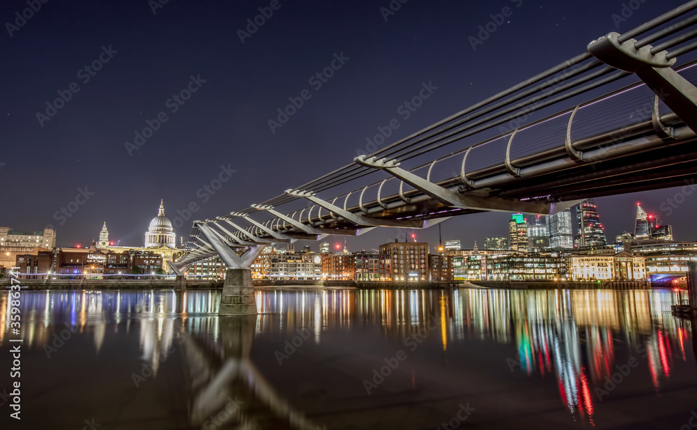 Millennium Bridge at Night in london looking over the river Thames towards st pauls Cathedral with reflections of the city lights. 