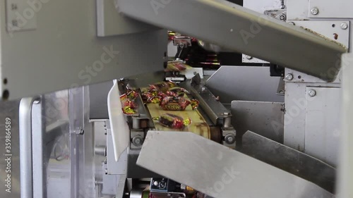Chocolate candies wrapped in candy wrappers move from the packaging machine along the conveyor.