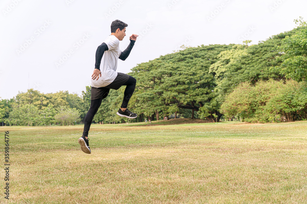 Handsome young man athlete runner with energy exercise training and jumping outdoors with big green tree in the public park. Active healthy and motivation lifestyle and ambition Concept Handsome young man athlete runner with energy exercise training and jumping outdoors with big green tree in the public park. Active healthy and motivation lifestyle and ambition Concept