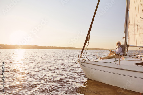 Wallpaper Mural View of the sail boat or yacht floating in sea with relaxed senior man reading a