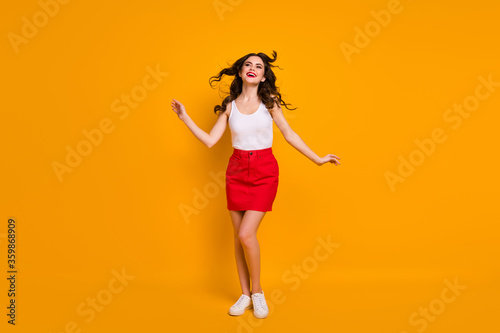 Full length photo of pretty lady hairdo flight satisfied look enjoy warm summer breeze wear white casual tank-top red short skirt shoes isolated yellow bright color background