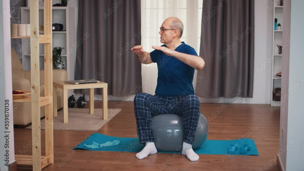 Senior man training on stability ball in living room. Old person pensioner healthy training healthcare sport at home, exercising fitness activity at elderly age