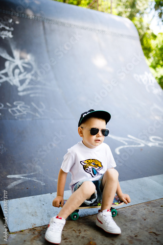 Boy with a skate in a skate park. The boy is sitting on a skateboard.