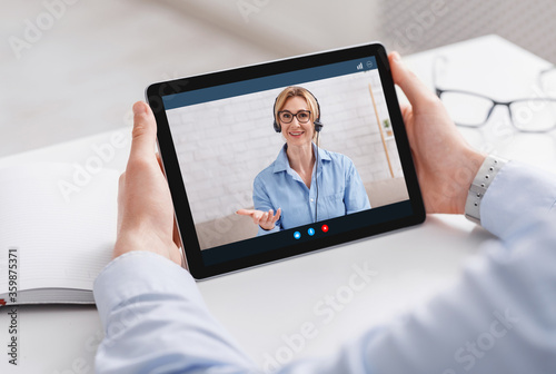 Online work and communication with consultant. Man holding tablet with video call of woman