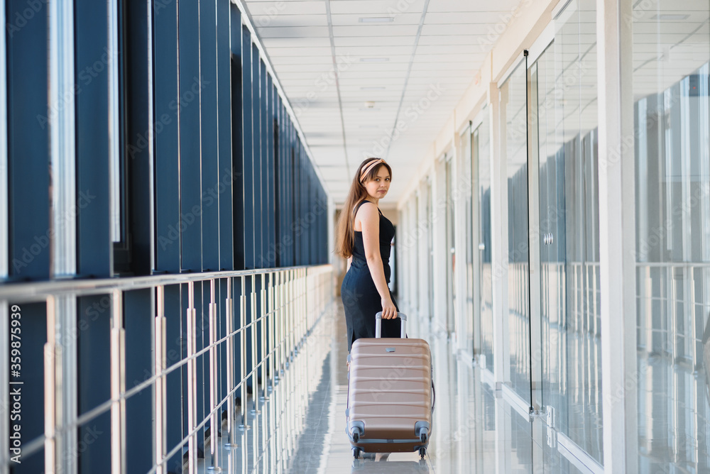 Stylish woman in a black dress with a suitcase in the airport terminal waiting for a plane.