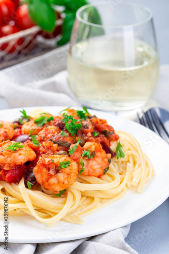 Italian dish shrimp linguine Puttanesca, pasta with shrimps in spicy tomato basil sauce garnished with parsley, vertical