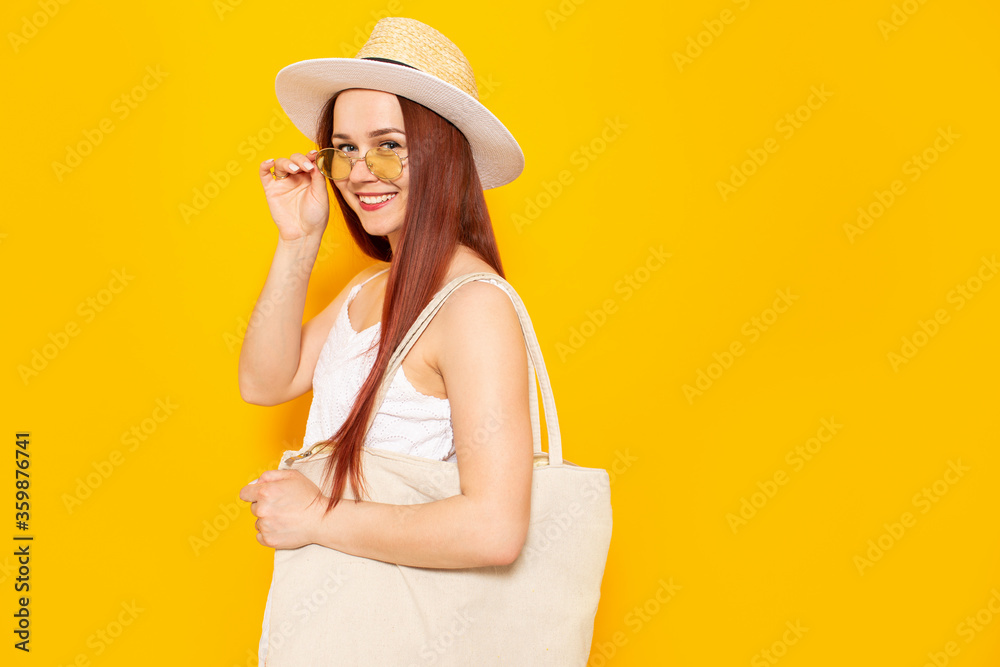 Young attractive woman in a white hat and white summer dress with eco shopping bag smiling on a yellow studio background. Young attractive woman in a white hat and white summer dress with eco shopping bag smiling on a yellow studio background.