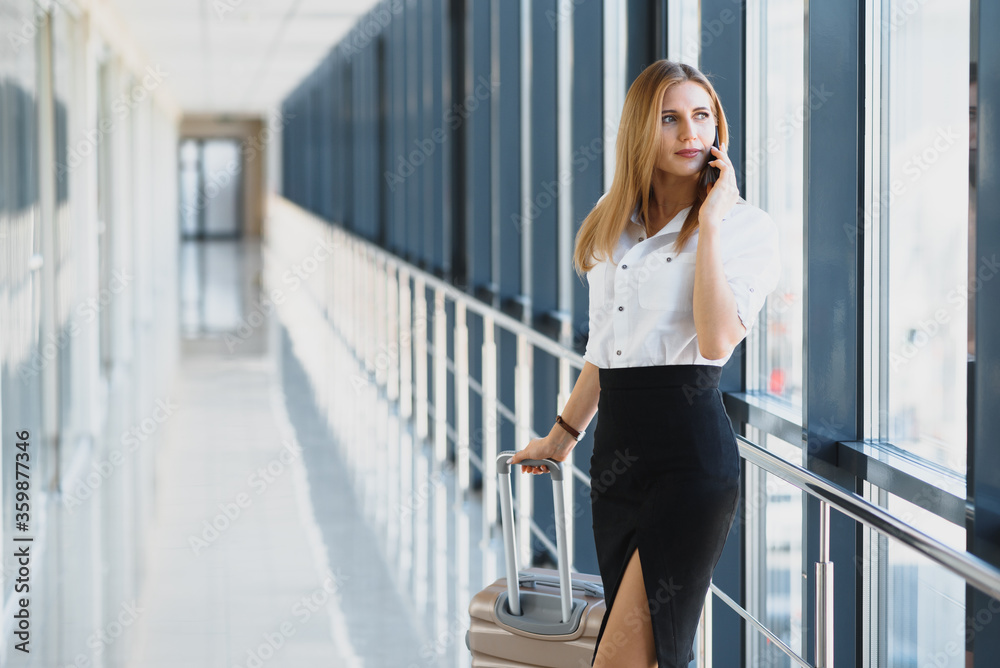 Portrait of young attractive businesswoman talking on smartphone with her suitcase in airport