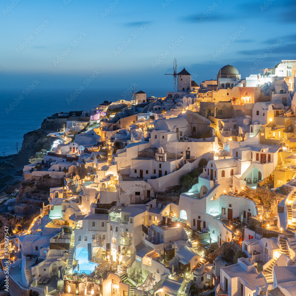 Oia in Santorini Greece taken at dusk looking towards the windmills and villas with swimming pools at night. 