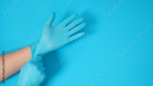hand is pulling doctor gloves or blue latex gloves of right hand on blue background.