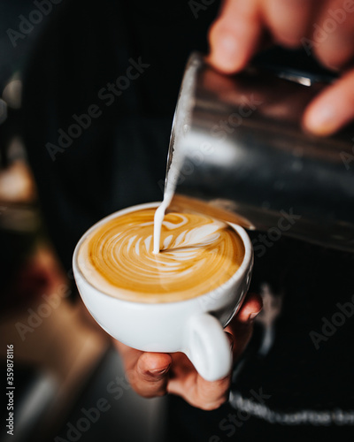 Professional barista pours white milk latte foam into a cup of coffee - the art of brewing excellent cappuccino