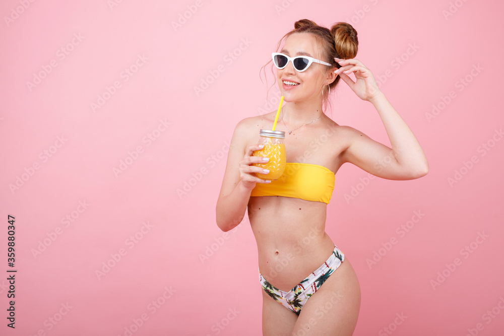 Naklejka premium girl smiles in a swimsuit and juice in a glass on a pink background. summer mood