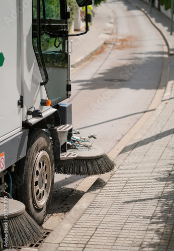 Sweeper truck industrial vehicle cleans urban streets of the city on urban service workers background. Fragment of a street cleaning machine. Conception of ecology and public services of the city.