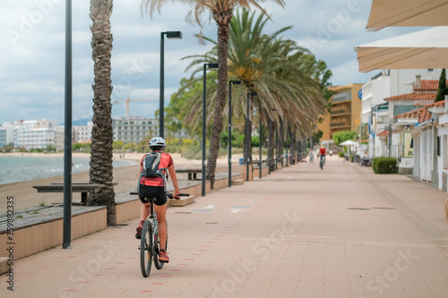Cyclist in helmet on a bike path on the promenade in a seaside town in the sunny day. Bicycle road sign and arrow on the sidewalk. Active and healthy lifestyle in the modern world. Roses, Spain.