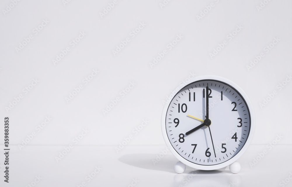 White round alarm clock in 8 o'clock on tabletop with white wall background White round alarm clock in 8 o'clock on tabletop with white wall background