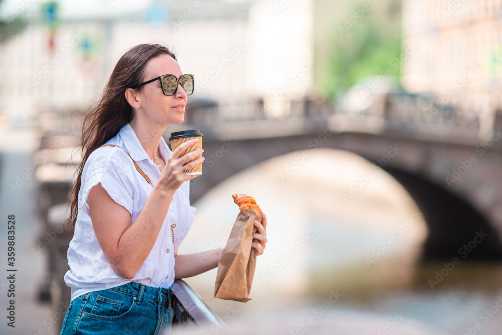 Woman with a croissant and coffee outdoors on the promenade Woman with a croissant and coffee outdoors on the promenade