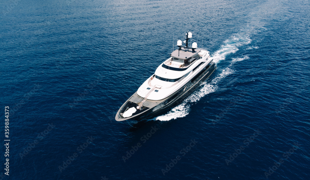 Fototapeta premium Aerial view of luxury yacht goes to open sea with beautiful blue colour of water. Wealth recreation lifestyle. Bird's eye view of expensive floating ship traveling by Europe in summer