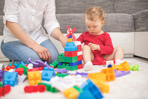 Child girl with mom play in multi-colored toy blocks and cubes.