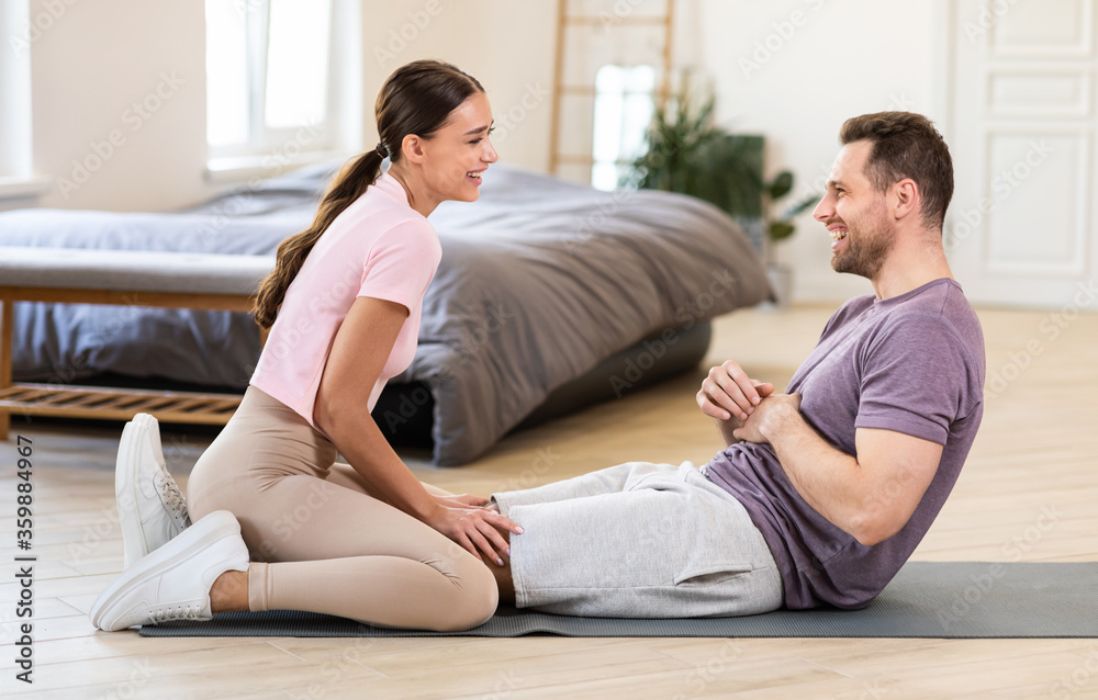 Girlfriend Sitting On Boyfriends Legs Helping Him Exercise At Home