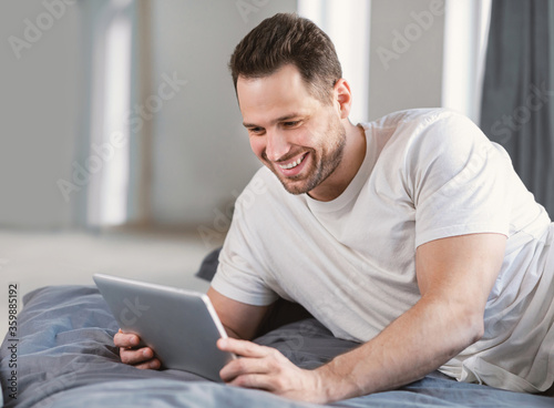 Man Using Digital Tablet Watching Movie Lying In Bed Indoors