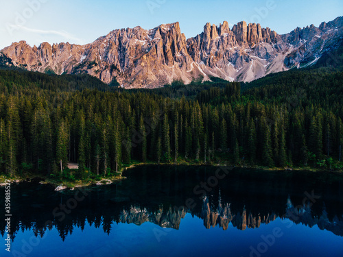 Fototapeta Naklejka Na Ścianę i Meble -  Picturesque peaks of Dolomites mountains in reflection of crystal clear pond surrounded by coniferous forest. Lake of Caresse in Italy. Scenic place and famous touristic destination. Primeval nature