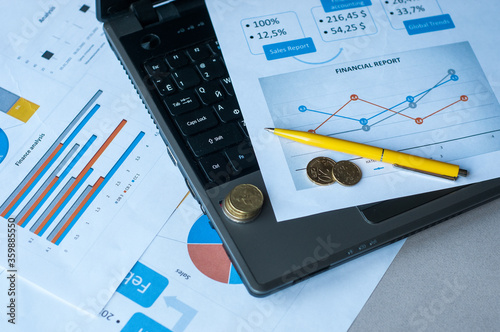 Selective focus of laptop, coins, papers, glasses, pen and calculator on table