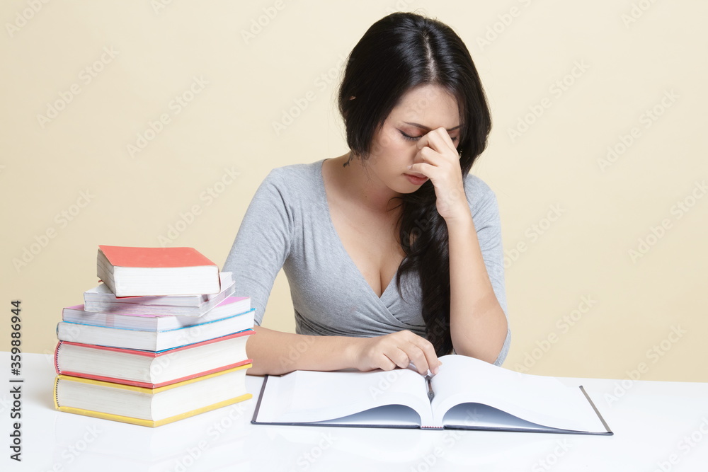 Exhausted Asian woman got headache read a book with books on table. Exhausted Asian woman got headache read a book with books on table.