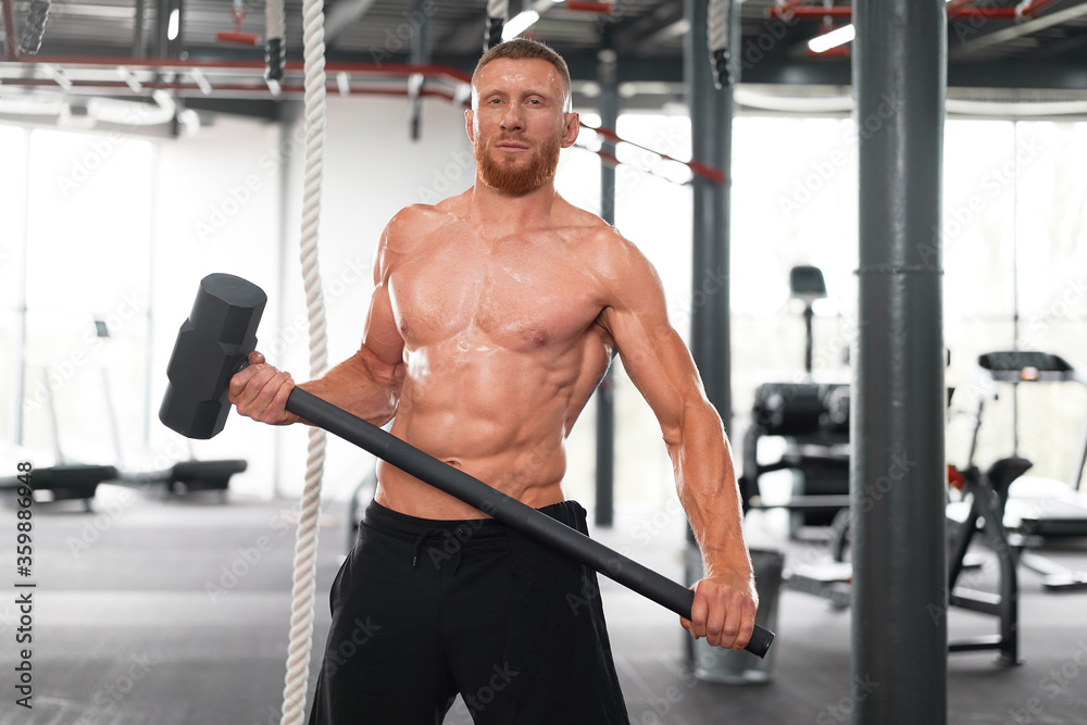 Fototapeta premium Man gym hammer hit tractor wheel hitting huge tire Athlete sportive man Middle adult handsome sportsman bodybuilder weightlifter ideal body