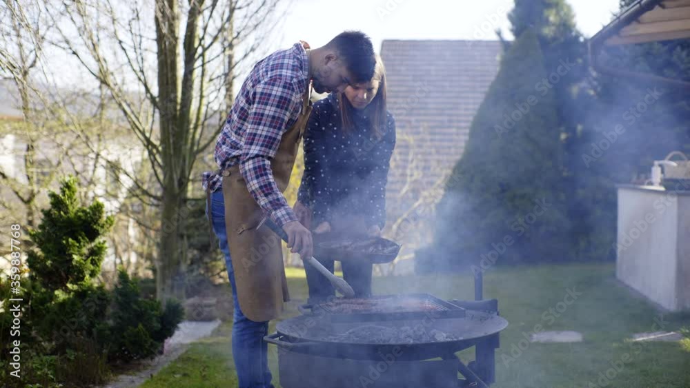 Man and woman collecting meat from the from the grill fire pit, smoke into camera Man and woman collecting meat from the from the grill fire pit, smoke into camera