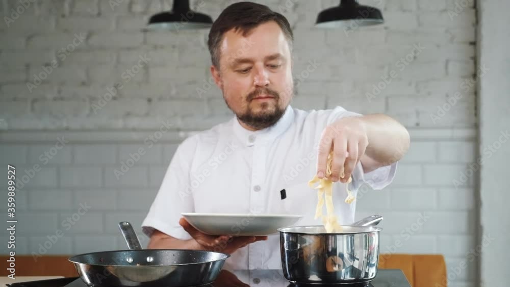 Chef is cooking italian pasta, he puts raw macaroni from plate to pan, bowl
