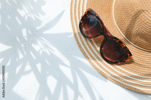 Straw hat and sunglasses in the morning with palm tree shadow and blurry background.