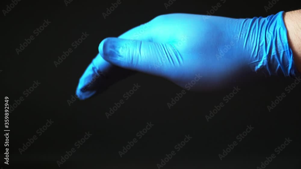 A man's hand in blue medical gloves on a black background