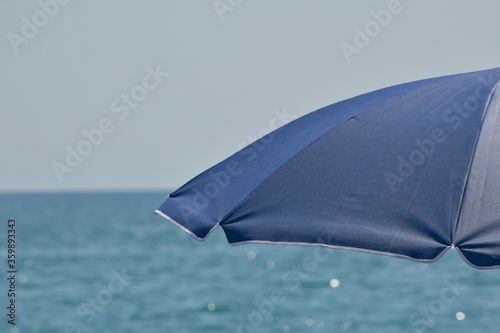 An open fragment of the visor of the blue umbrella without a leg awning against the sea.