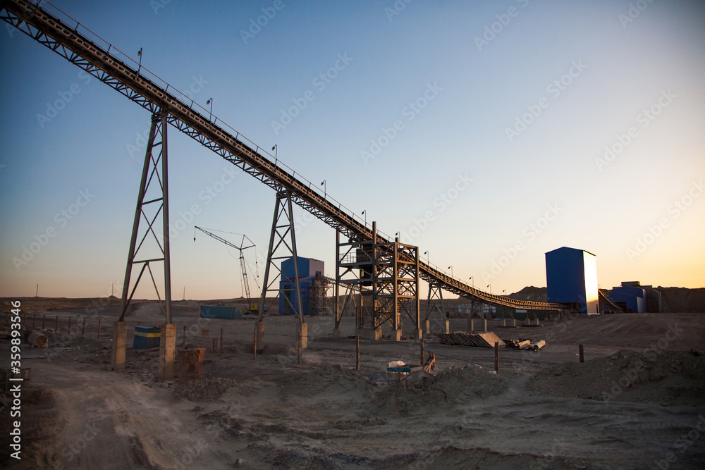 Gold mining and processing plant. Transporter (conveyor belt) and silo on gold ore quarry. Yellow warm tones on sunset.