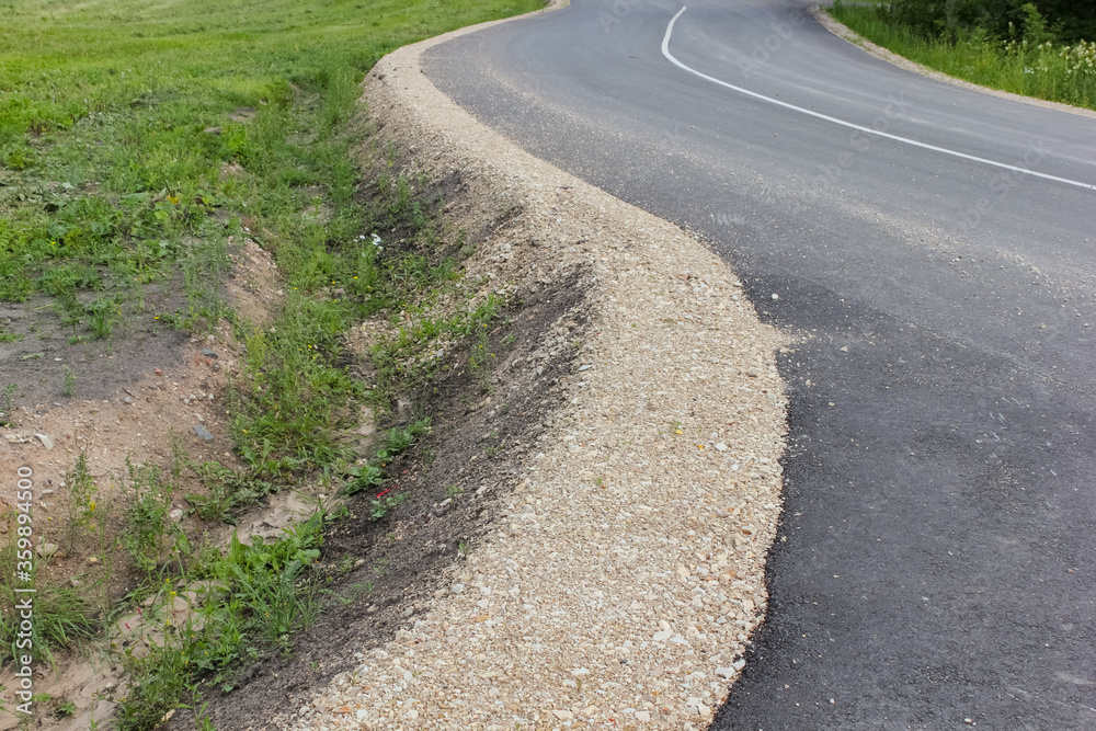 View to a winding new asphalt road in a rural area. Gravel roadside, ditch for rainwater. Latvia. View to a winding new asphalt road in a rural area. Gravel roadside, ditch for rainwater. Latvia.