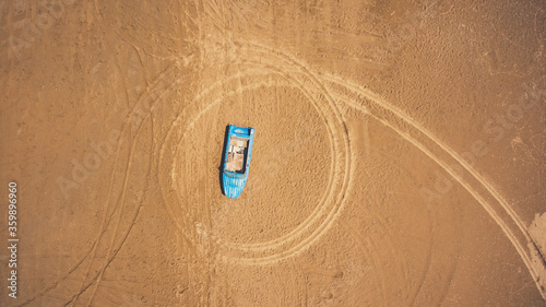 Top view aerial photo from flying drone of a blue boat on a beach in Thailand in sunny summer day. One wherry is lying on a sand with copy space for your travel blog photo