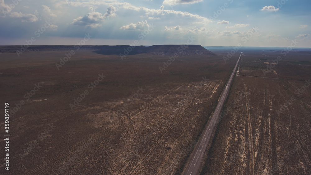 Fototapeta premium Aerial photo from flying drone of a beautiful nature landscape with asphalt road in Texas district. View on a way in countryside and silhouette of mountains against cloudy sky with sun rays