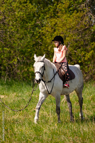 Little European girl rides a white horse