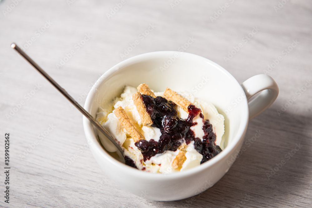 Vanilla ice cream with blackberry jam in a white cup on a wooden light background Vanilla ice cream with blackberry jam in a white cup on a wooden light background